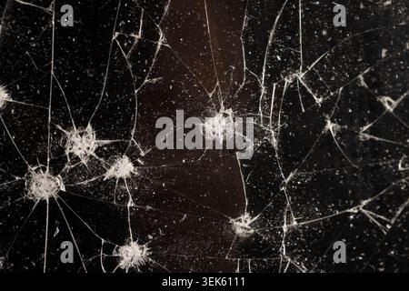 broken glass on black paper, dents and dots on the glass where it broke, white cracks and completely broken places on the glass on a black uneven back Stock Photo