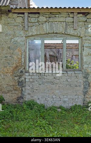 Old, weathered window set into a dilapidated stone and brick wall. The window has multiple panes and appears to be in a state of disrepair. Stock Photo