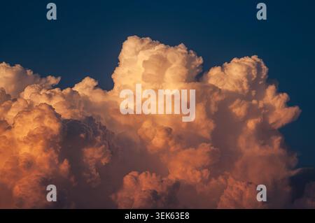 Dramatic sunset clouds illuminated by golden hour light against a deep blue sky Stock Photo