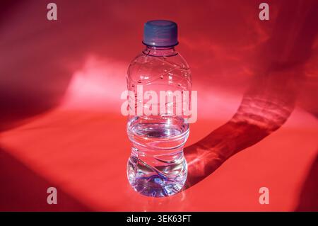 Clear plastic bottle filled with water casting a dramatic shadow on red background Stock Photo