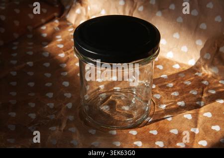Empty glass jar with black lid on patterned paper with heart shapes Stock Photo