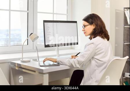 Female doctor in clinic office using laptop and monitor for patient data Stock Photo