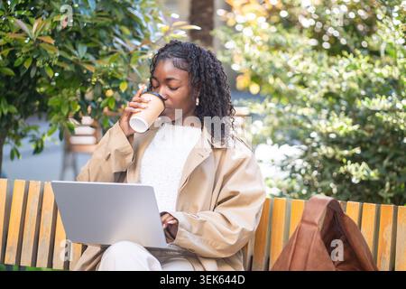 Relaxed carefree african american woman freelancer drinking coffee while comfortably works on laptop Stock Photo