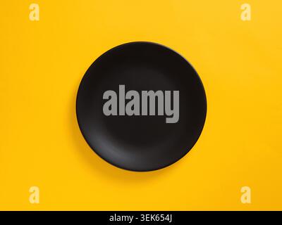 Black plate on yellow background, minimalist composition offering copy space for culinary or design themes Stock Photo