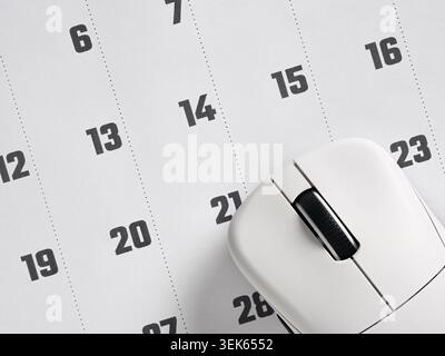 White modern wireless mouse positioned on a minimalist calendar page, representing digital scheduling and appointment booking Stock Photo