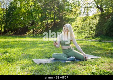 Blonde woman using smart phone during outdoor sport training in green Stock Photo