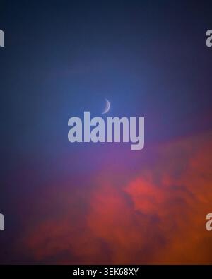 Waxing crescent moon above vibrant sunset clouds Stock Photo