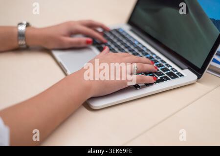 A close-up, shallow depth-of-field shot of a professional woman's hands using a mouse, keyboard, and laptop. This image emphasizes the "human-to-tech" Stock Photo