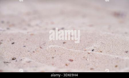 Sand patterns on beach with small stones and shells at low tide during daylight near ocean waves Stock Photo