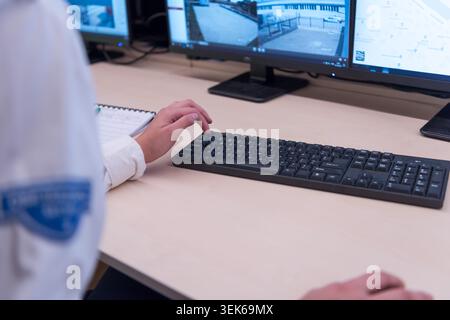 Close-up of a female security dispatcher or guard in uniform writing notes and filling out an incident report sheet or daily logbook at her desk next Stock Photo