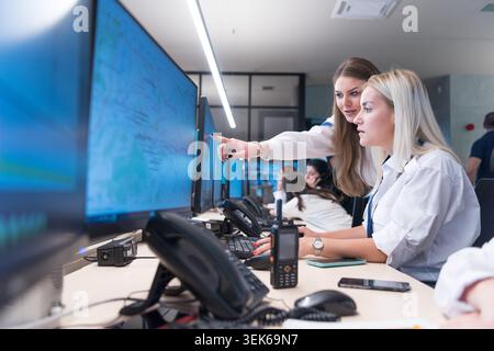 A male security manager and two female guards looking at desktop computer screens together, discussing data and collaborating inside a large surveilla Stock Photo