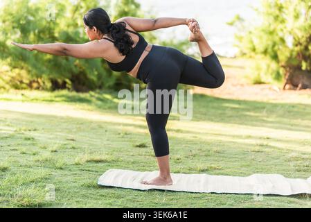 Woman practicing advanced yoga king dancer pose on an outdoor mat Stock Photo