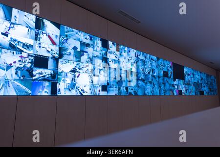 Wide angle view of a massive grid of video screens showing various indoor and outdoor real-time surveillance footage inside a modern security command Stock Photo