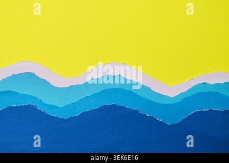 Layers of torn paper in various shades of blue and white, arranged to evoke rolling ocean waves. on vibrant yellow background. Stock Photo