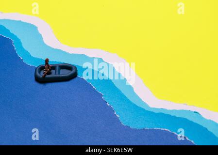 Miniature Person Seated In Small Dinghy Boat Floating On Blue Wavy Water Against Yellow Sky Backdrop Stock Photo