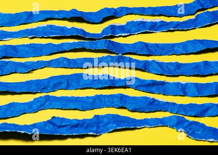 Abstract Textured Torn Blue Paper Strips on Bright Yellow Background Stock Photo