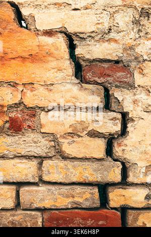 Cracked old brick wall texture with weathered mortar and peeling plaster on vintage urban facade, vertical Stock Photo