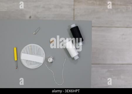 Sewing supplies are placed on a table ready for crafting. There is thread, needles, a button, a safety pin, and other tools. All items are organized f Stock Photo