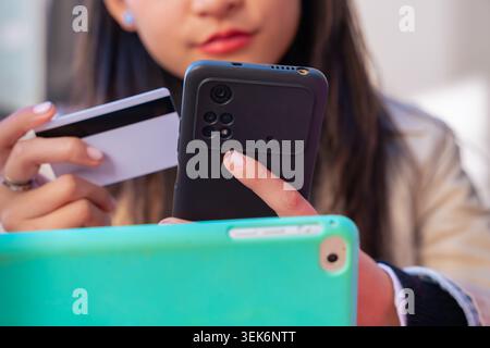 Young woman holding credit card and smartphone making online payment at home Stock Photo