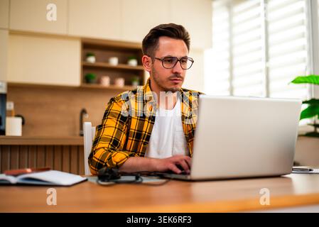 A freelancer works on his laptop, surrounded by a notebook and desk items in a modern home workspace. Stock Photo