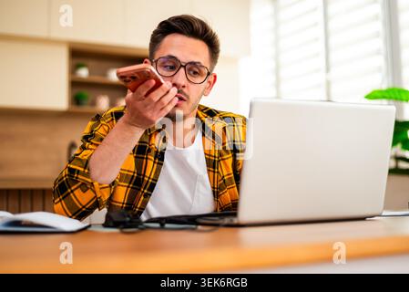 A young man sits at his laptop while carefully listening to a voice message or taking an important call. Stock Photo