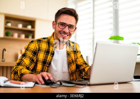 With a cheerful expression, a man uses his laptop, appearing to analyze information or solve a problem online. Stock Photo