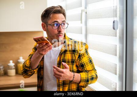 Looking through window, a man in a yellow plaid shirt talks on his smartphone. Stock Photo