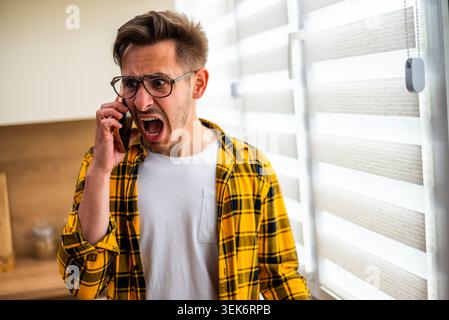 Young man is talking on phone at his home. He appears angry and distraught. Stock Photo