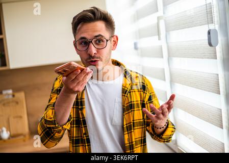Standing near a window, a man in a yellow plaid shirt talks on his smartphone. Stock Photo