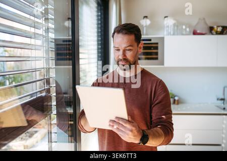 Man using smart home app to control electric window shades indoors. Stock Photo