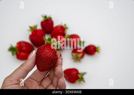 Ripe strawberries displayed in a handmade wicker tray on a white table with a soft green background. Ideal for organic food, summer harvest, healthy l Stock Photo