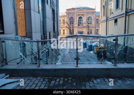 A stark close-up, low-angle perspective looking through a severely shattered glass windowpane spiderwebbed with sharp cracks and holes. Stock Photo