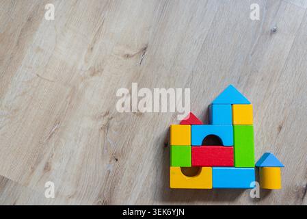 top view of small house built from colorful wooden toy blocks on a light wooden background, with large copy space, for real estate, finance or Stock Photo