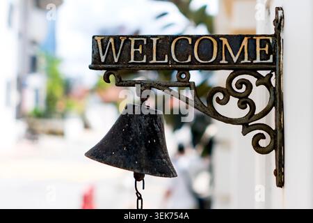 An antique-style, rustic cast iron "WELCOME" sign mounted on a wall, featuring an attached hanging bell with a chain. The background shows a beautiful Stock Photo