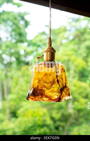 A rustic, textured amber glass pendant light fixture with a brass socket hanging outdoors. The warm-toned decorative lamp stands out beautifully again Stock Photo