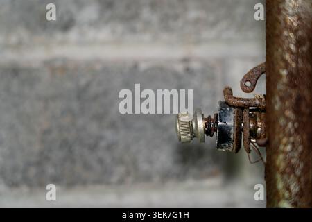 A detailed close-up shot of an old, weathered mechanical knob with a spring mechanism and rusted wire attachments. The object extends from the right s Stock Photo