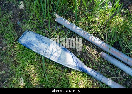 A top-down view of a worn-out blue plastic paddle and broken metal poles forgotten on the grassy ground. A close-up shot showcasing textures of vintag Stock Photo