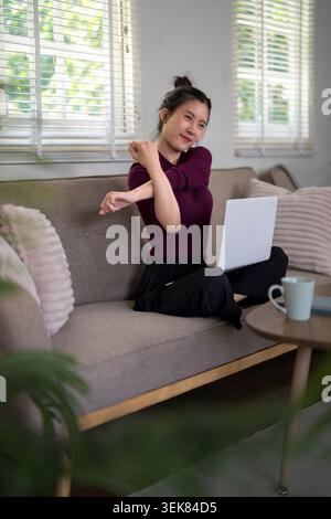 Asian young women stretching arms taking break from laptop computer working at home office on sofa with natural window Stock Photo
