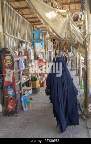 Woman wearing a blue burka walking along a bustling street in bamyan, passing market stalls with various goods. Stock Photo