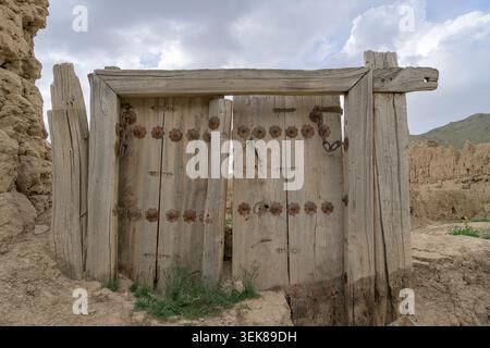 Ancient wooden double doors standing in a crumbling mud brick wall, showing traditional architecture Stock Photo