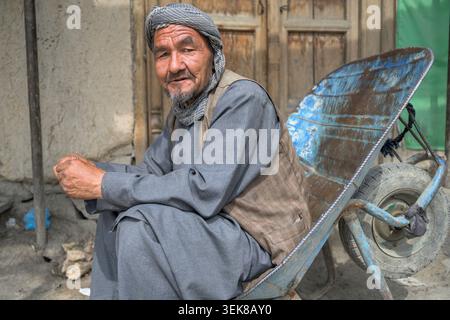Elderly man with traditional clothing sitting on a wheelbarrow looking at the camera Stock Photo