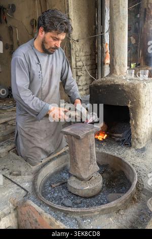 Blacksmith shaping hot metal by hand with a hammer and anvil next to a forge Stock Photo