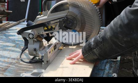A carpenter's hands working on a circular table while cutting a wide wooden board, a close-up of the process of processing and cutting building board Stock Photo