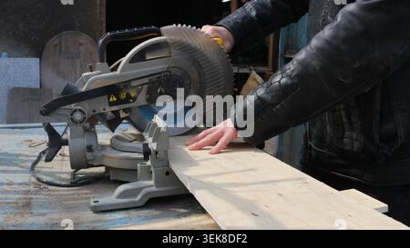 The miter saw is mounted on a workbench. The saw blade is partially lowered and covered by a protective guard. Yellow controls and safety warning sign Stock Photo
