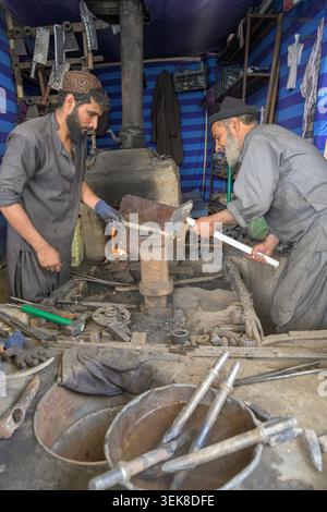 Blacksmiths are working together, shaping hot metal using traditional tools in their workshop Stock Photo