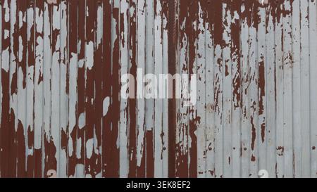 A metal surface with peeling paint. On the left is a large spot where the reddish-brown paint has peeled almost completely, revealing smooth Stock Photo
