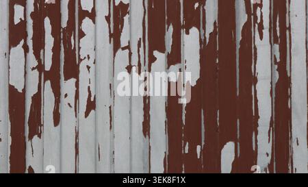 Distressed painted metal surface in fence or railing structure, white peeling paint on aged dark red iron textured background full frame close-up Stock Photo
