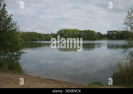 Peaceful lake surrounded by forest with reflections on the water and a small sandy shoreline. Natural landscape photographed during spring in the Czec Stock Photo