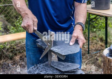 Traditional slate working: a slate slab is trimmed along its natural cleavage plane using a slate adze – a craft demonstration at an activity station during the 14th Frankenwald Hiking Marathon, Steinbach am Wald, Bavaria, Germany Stock Photo