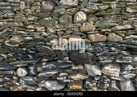 Full frame background texture of a traditional rustic dry stone wall, built with irregularly shaped grey and brown rocks stacked tightly together in b Stock Photo